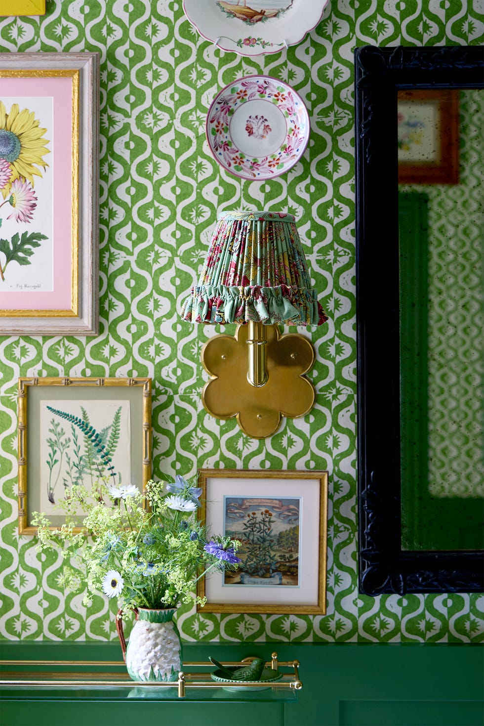 Decorative wall with patterned wallpaper, artwork, and a lamp.