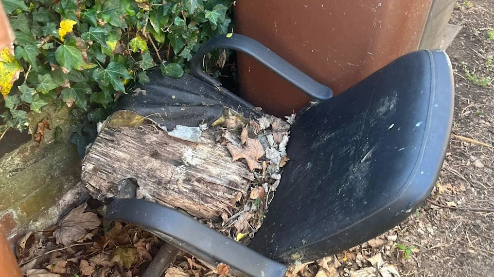 A rotting office chair left in an alley by a bin