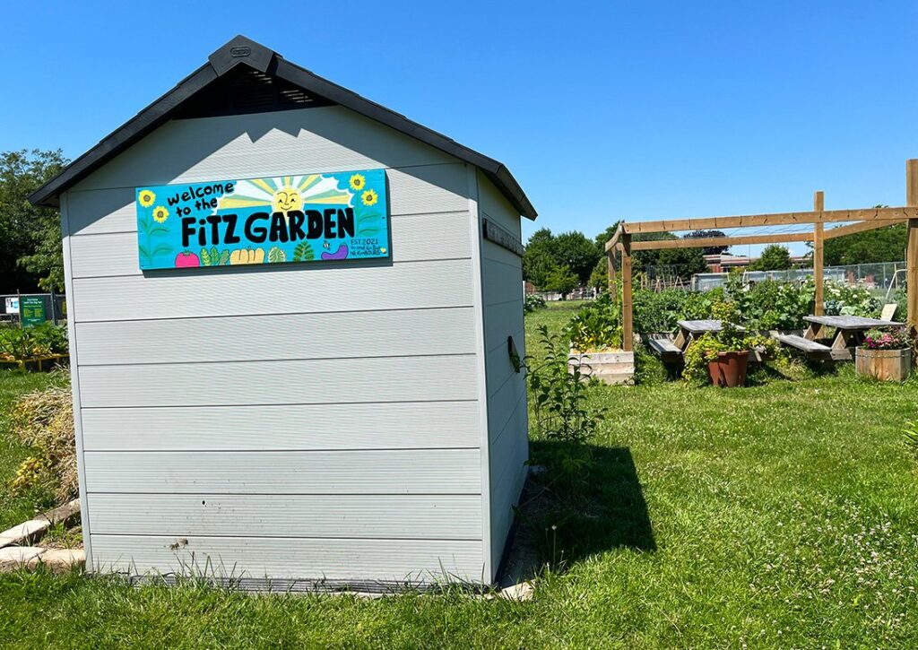 A storage shed with a sign that says, Fitz Garden, in front of the Fitz Community Gardens.