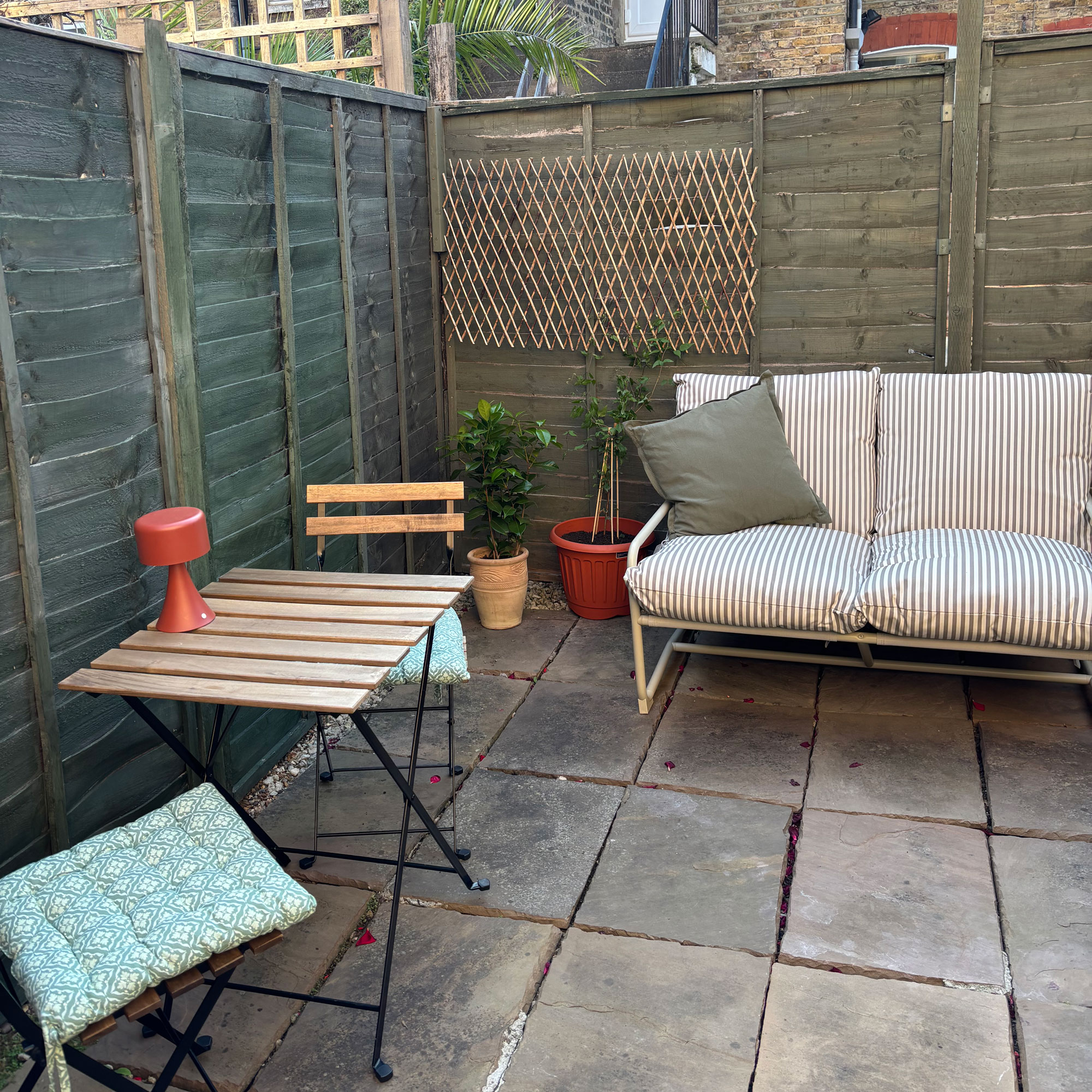 Green stripe sofa in a small green courtyard garden with a wooden table and chair