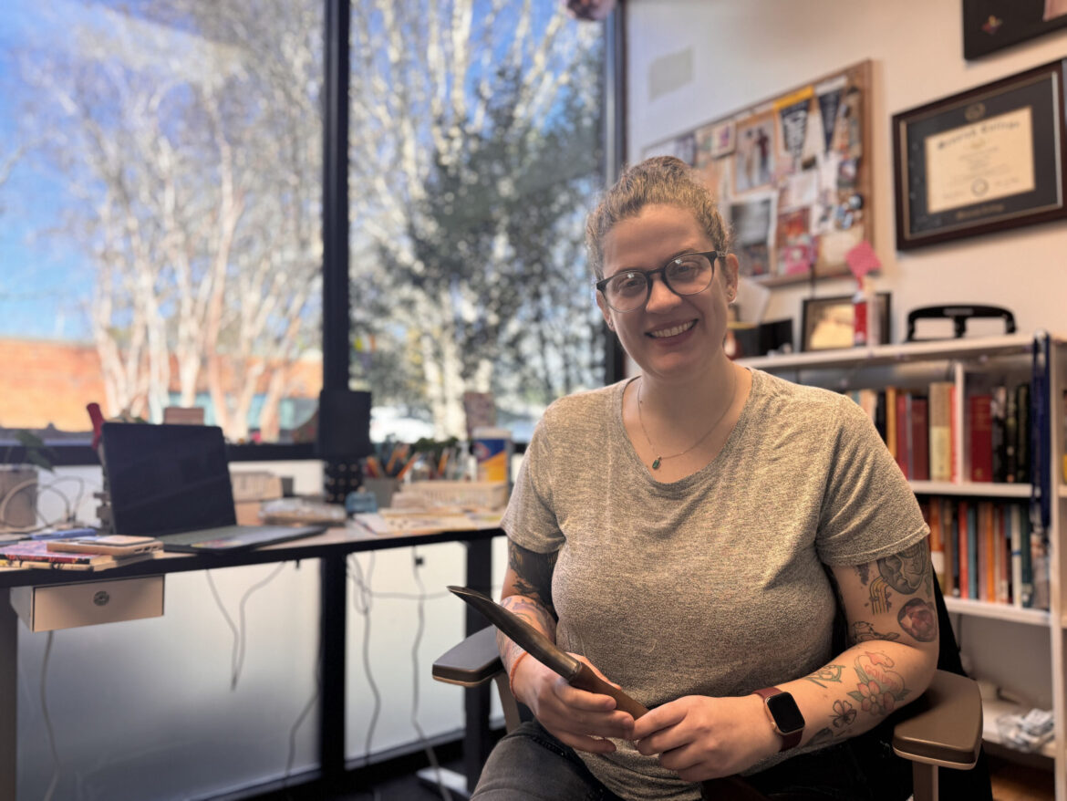 The Table at UGA Brings Guns to Gardens Event to Athens — Grady Newsource Woman sits with a garden tool in her hand at a desk and smiles at the camera