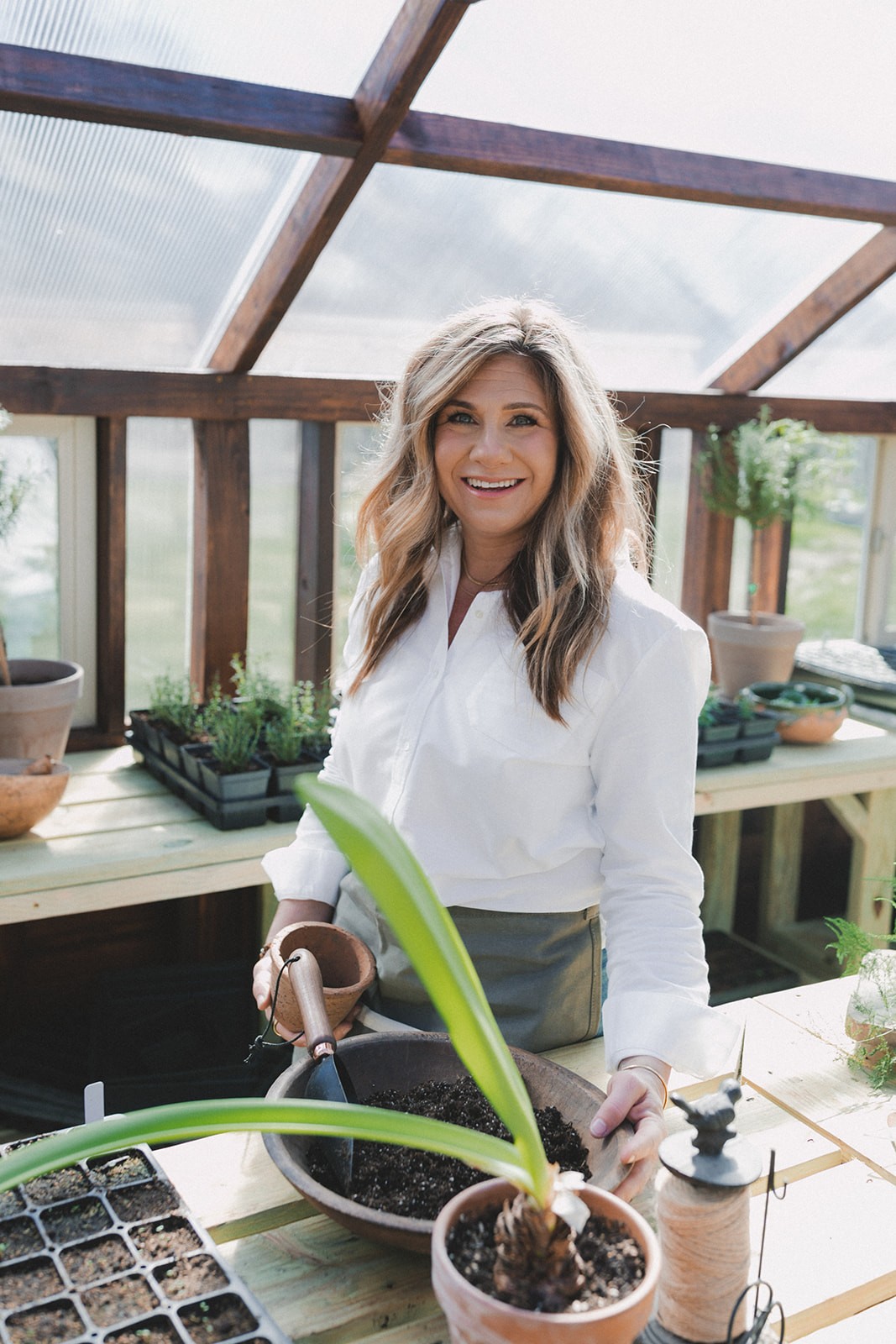 Woman with long blonde hair standing in a greenhouse.