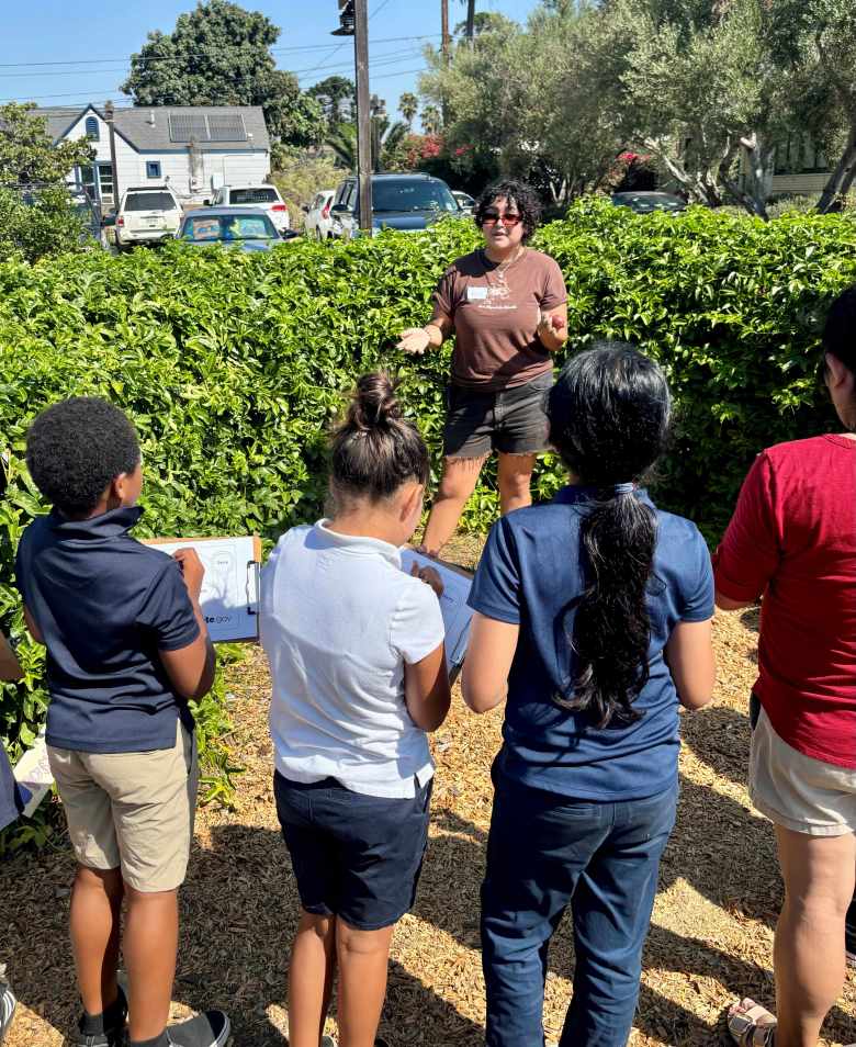Children listen to an instructor and take notes in a garden