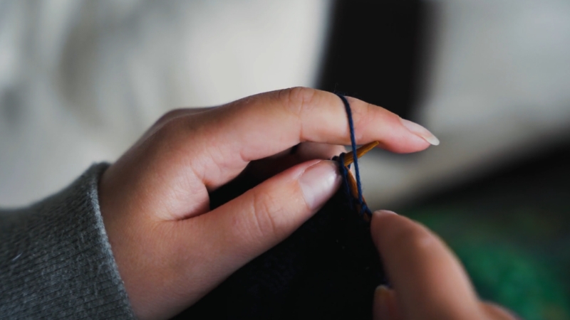 Close-up of hands knitting with dark yarn and wooden needles