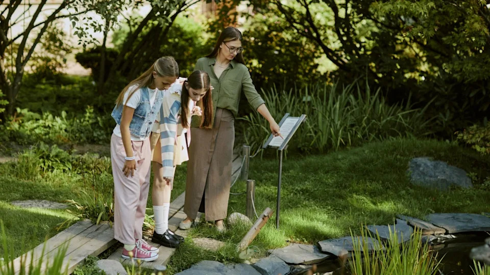 High angle view of young woman working in botanical garden showing aquatic plants to teen girls.