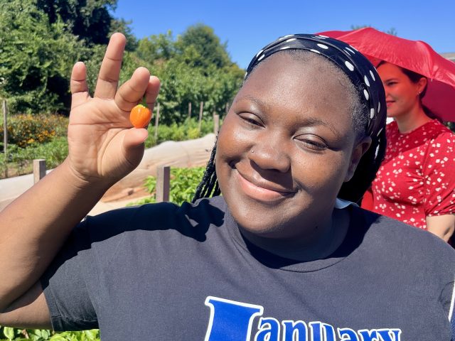 Bennett College student smiles while holding a freshly harvested pepper in a campus garden.