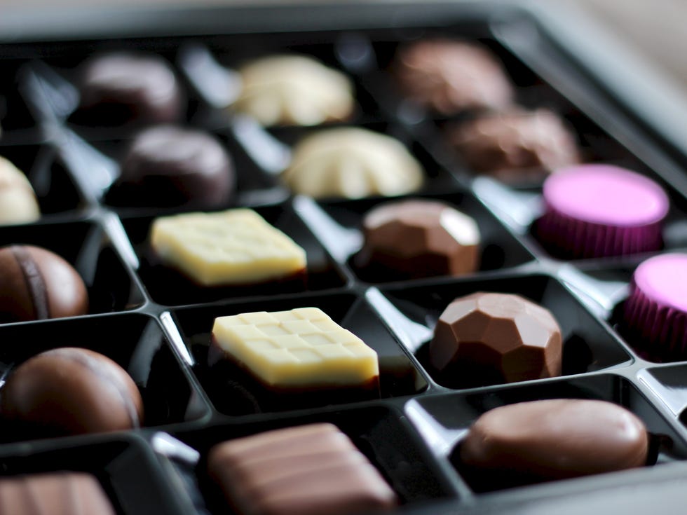 close up of assorted chocolate candies in a gift box. selection of gourmet milk, dark, and white chocolate bonbons. luxurious assortment of mini chocolate truffles and pralines. variety of chocolates with different flavors and shapes in black tray.
