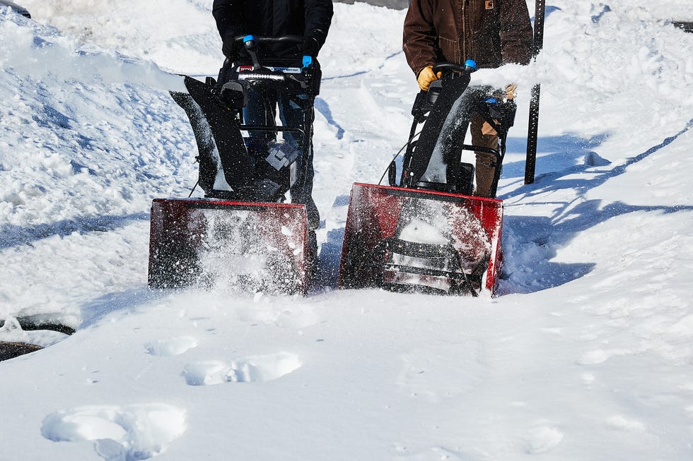 Two people using snow blowers in a snowy environment.