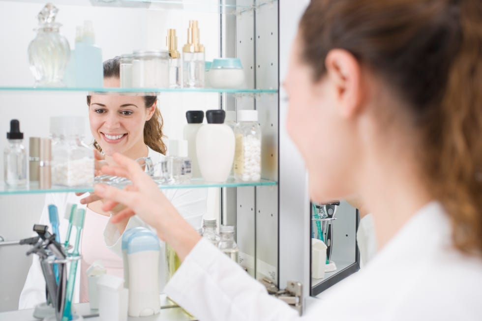 a smiling woman in white organizing items in a mirrored cabinet filled with beauty products