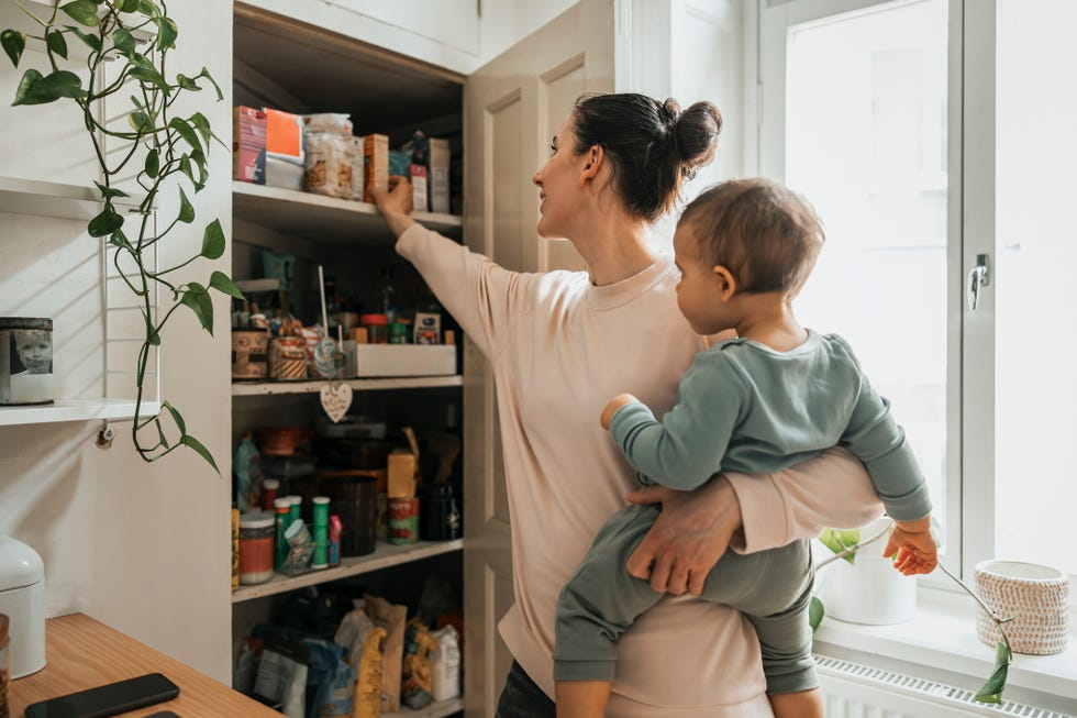 mother carrying baby boy removing ingredient from neat pantry in kitchen at home