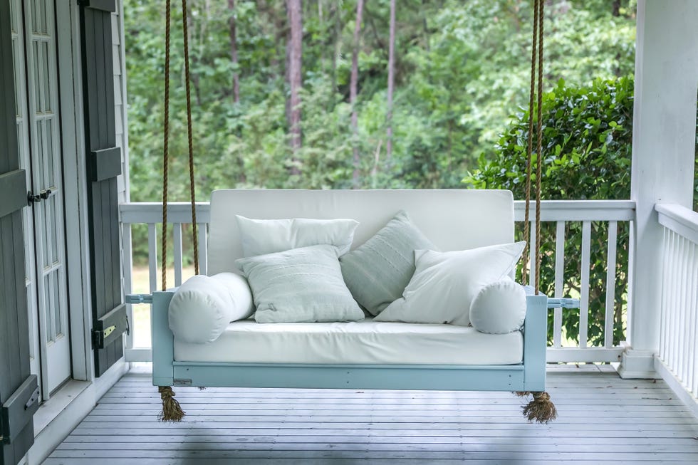 a luxurious and classic outdoor bed swing painted a seafoam green with white deep cushions and the swing is hung from the ceiling by rope.