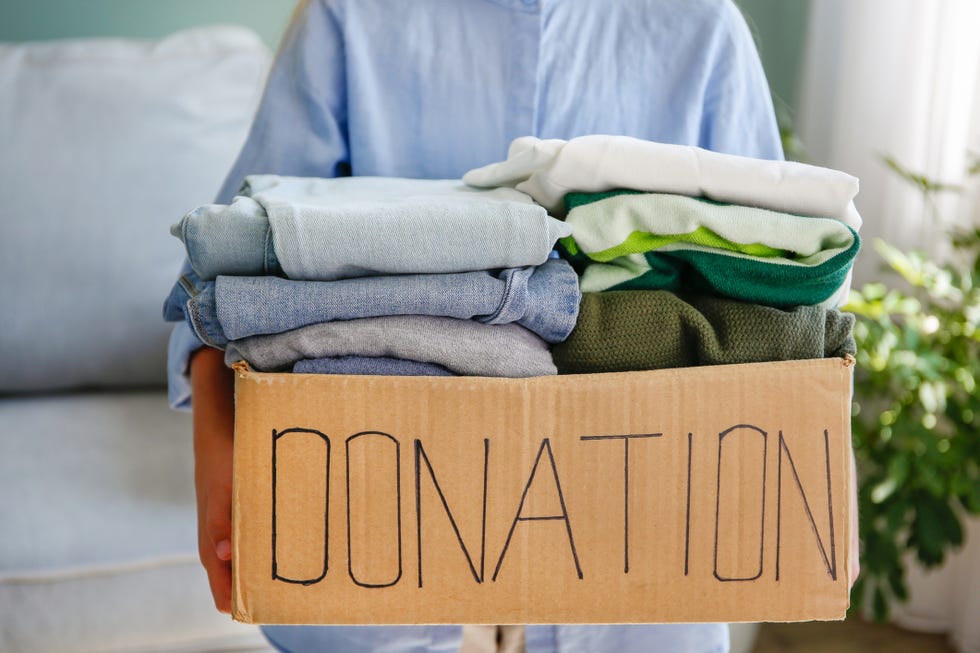 girl holding donation box with blue green and gray folded clothes