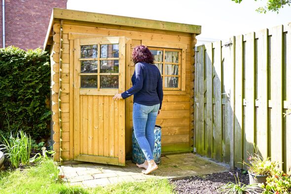 Woman opening the door of a wooden shed in her backyard garden