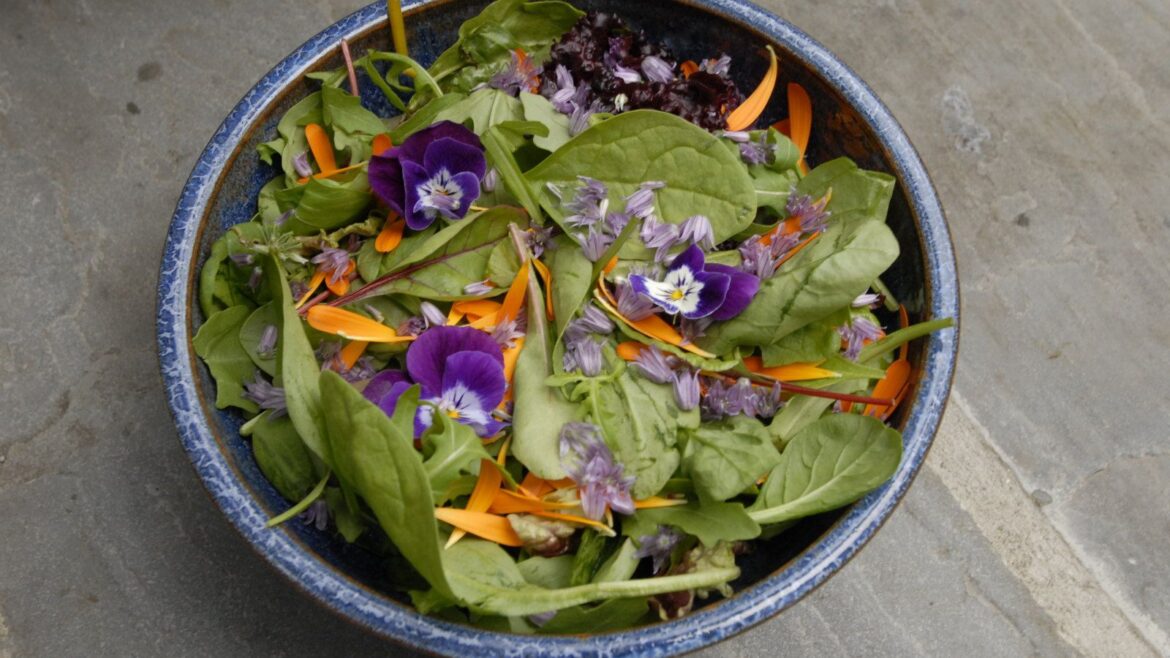 A salad bowl with edible flowers as decoration on a wooden table