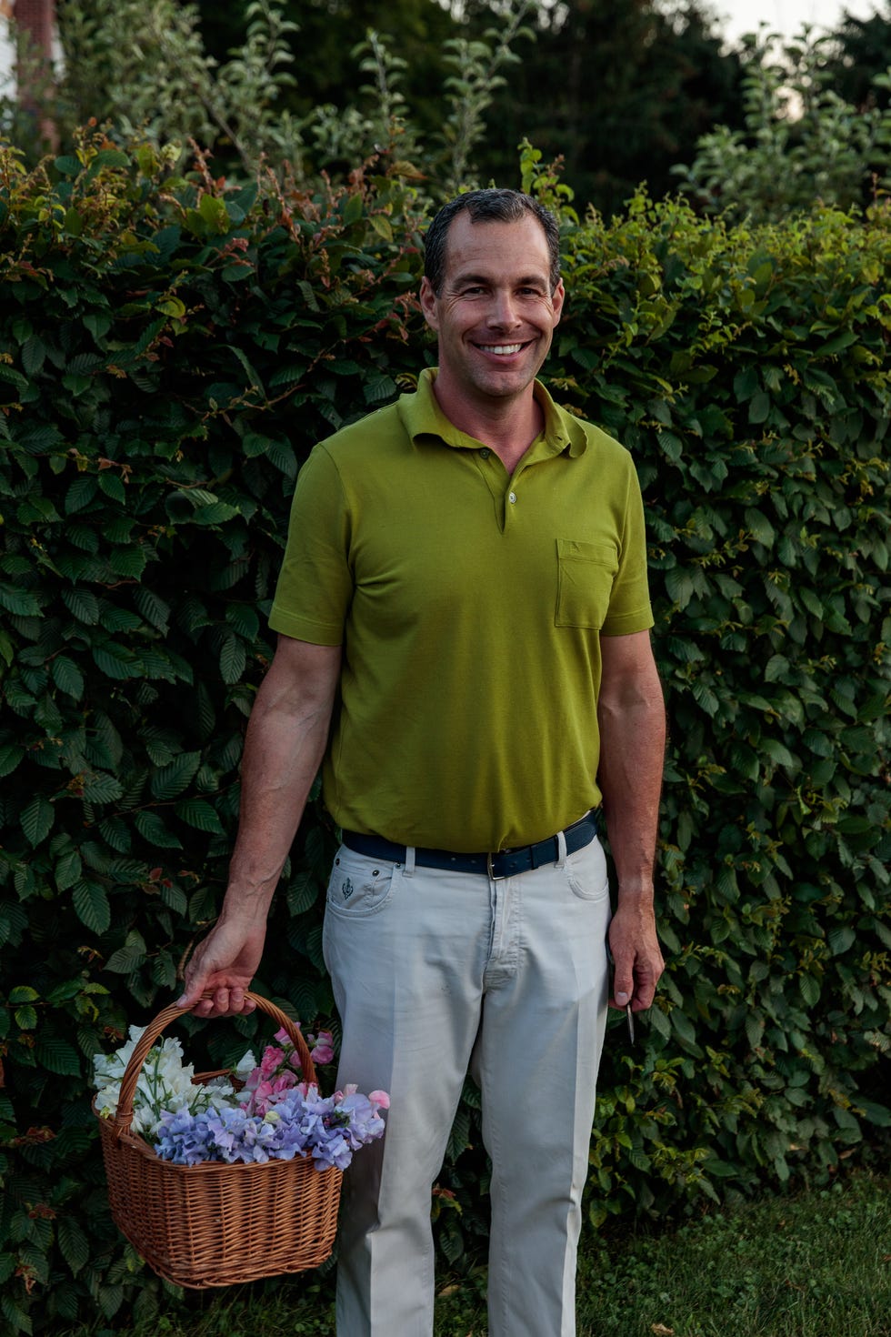 christopher spitzmiller holds a basket of sweet peas against a shrub wall