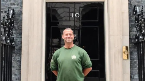 Smiling Karl Stevens, wearing a green gardening jumper, poses outside the door of No.10 Downing Street
