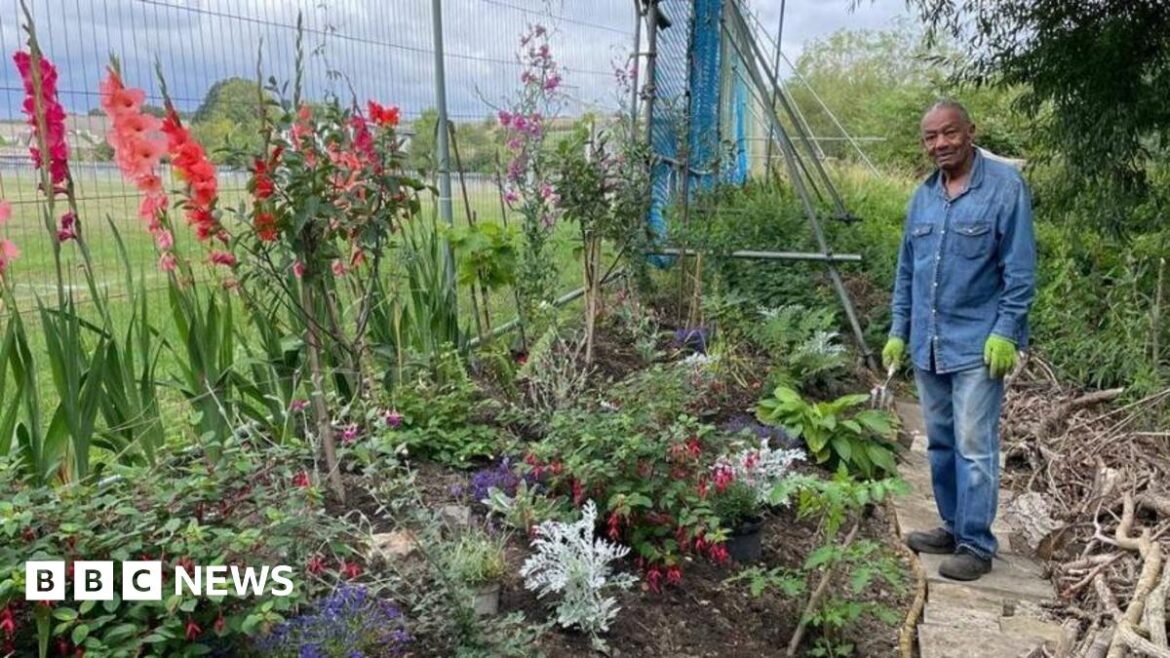 A man stood next to a planter containing plants and flowers inspired by Caribbean heritage.