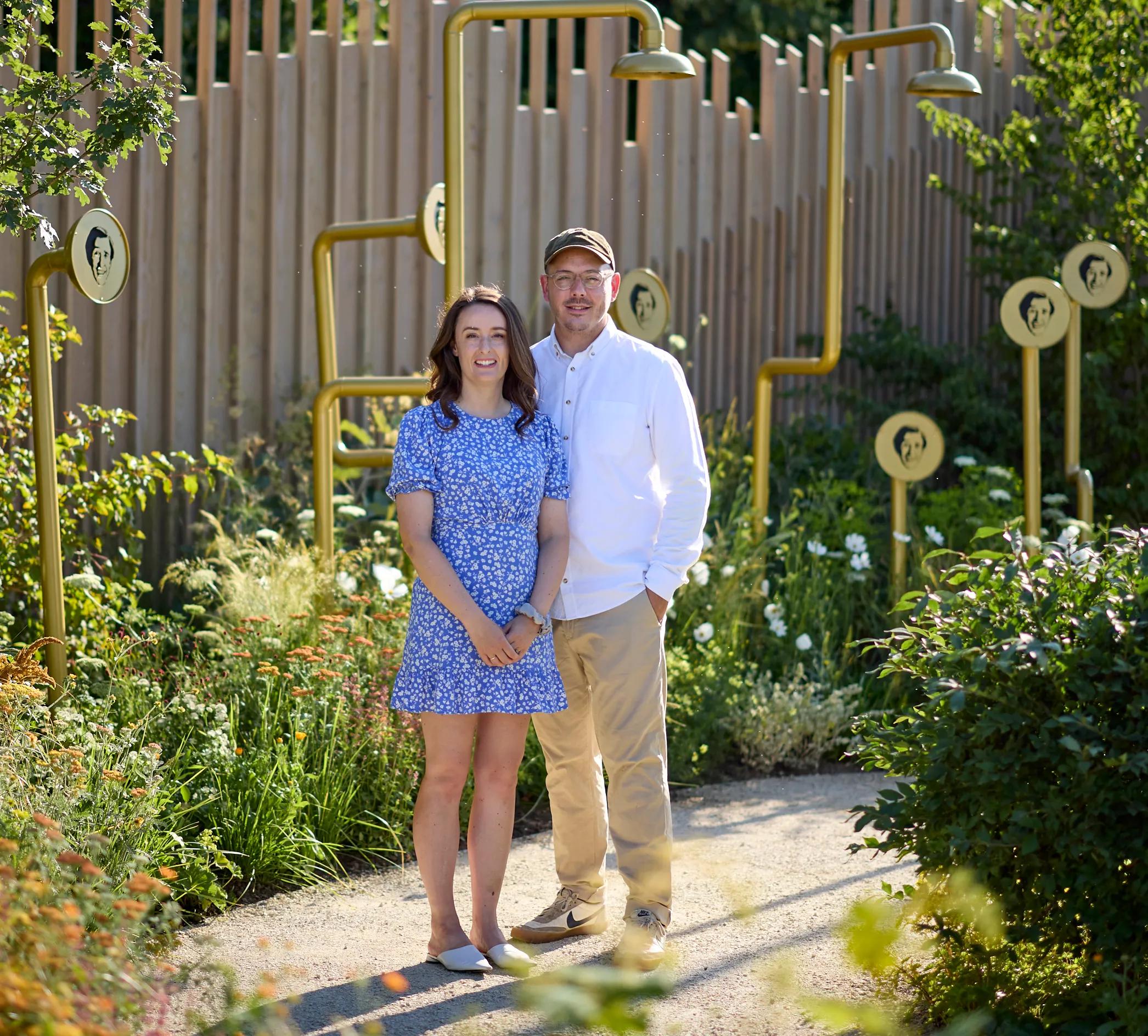 Joe and Laura Carey, garden designers, posing in their garden design with golden shower heads.