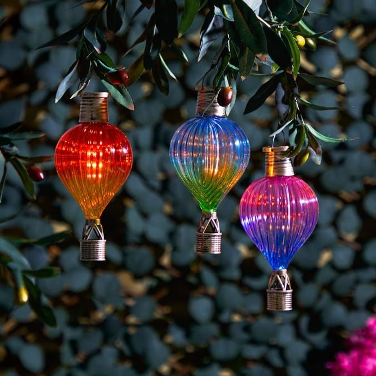Three colourful Firefly Solar Light Co Clip-On Hot Air Balloon Lights hanging from a tree 