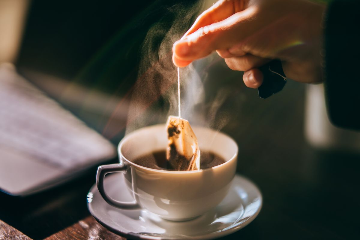 Hand is picking a tea bag out of a white cup.