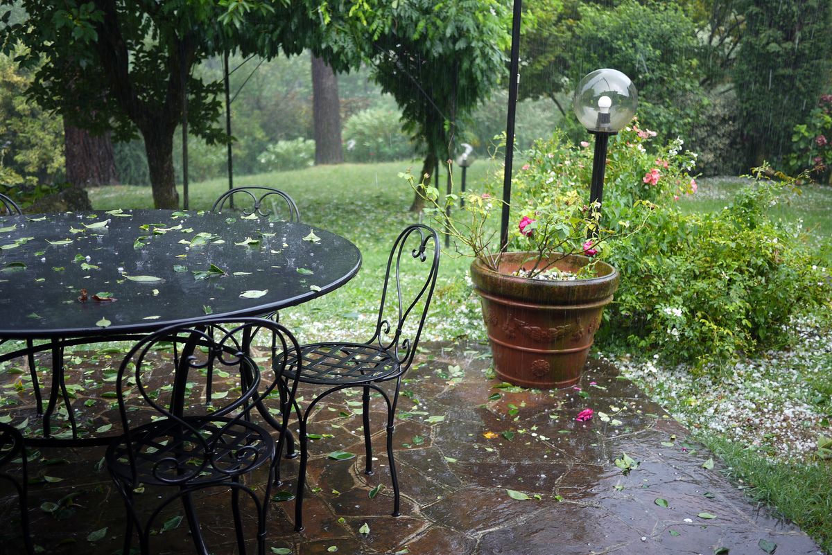 Italian garden during a heavy hail storm, fallen leaves all over. Trees and bushes in the background. Flower pot with red roses, garden lamp.