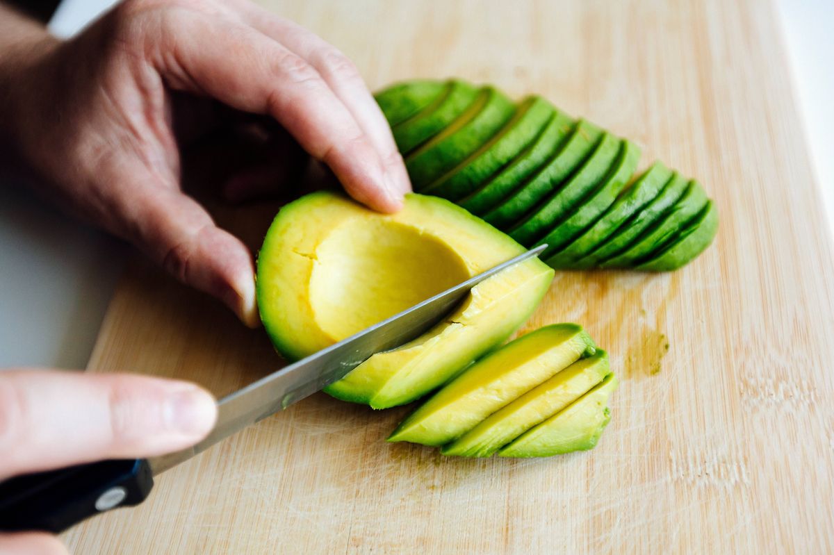 Man slicing avocado with a knife on a cutting board close up