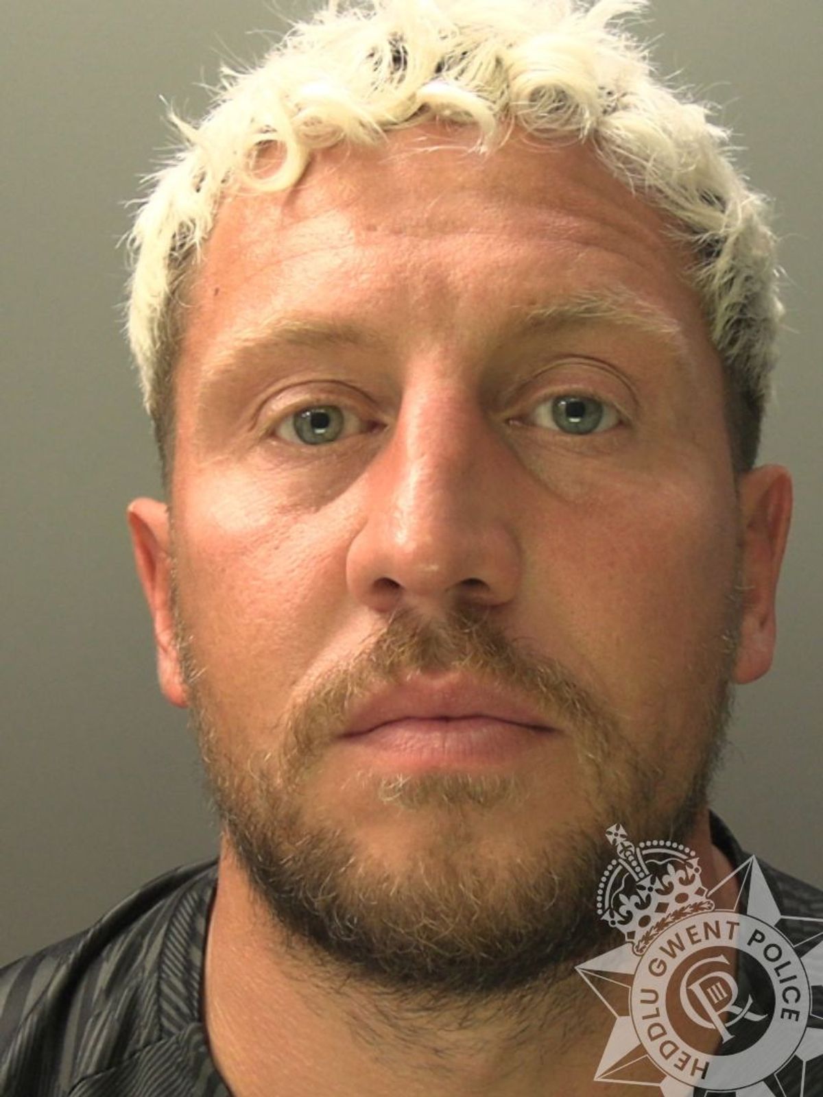 Custody photo of Bradley Williams, 38, who has bleached hair, a brown beard and is wearing a black t-shirt.