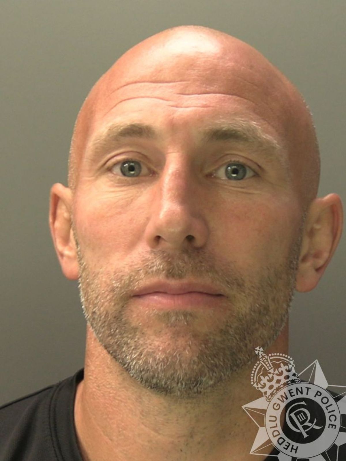 Custody photo of Danny Tomlin, 40, who is bald, has grey stubble and is wearing a black t-shirt.