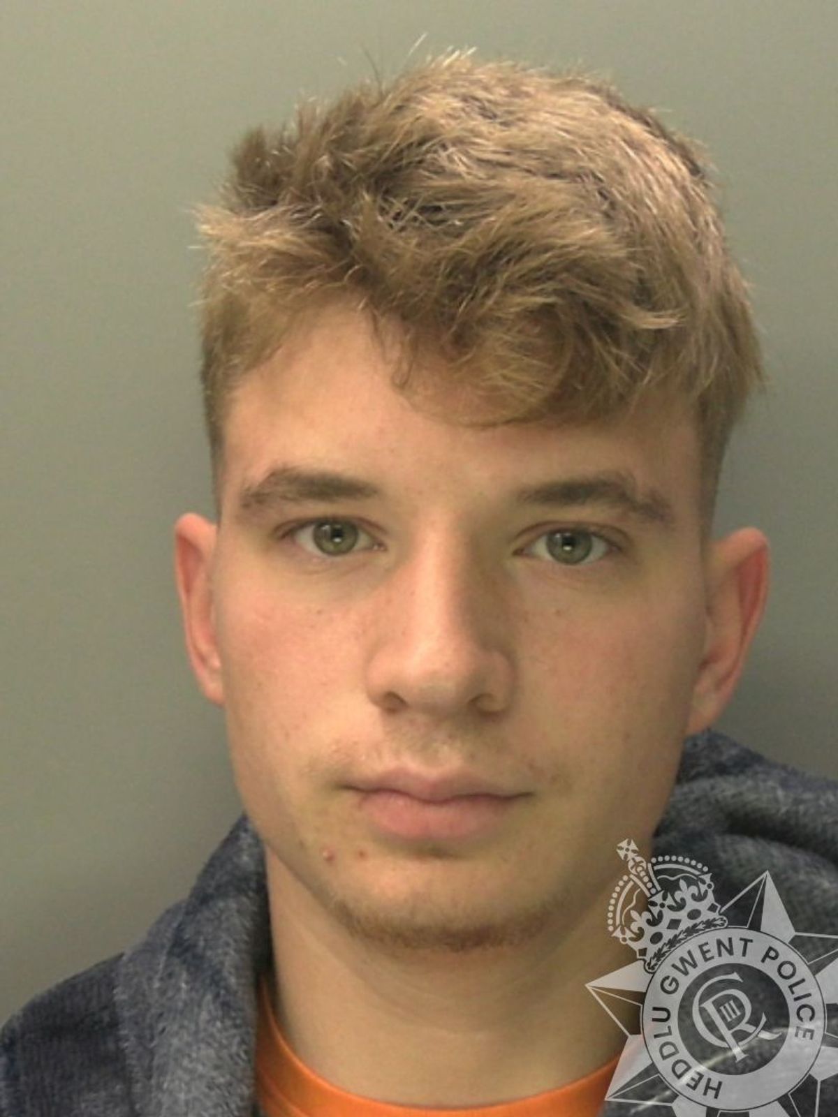 Custody photo of Jack Griffin, 21, who has blonde hair, and is wearing a grey hoody and an orange t-shirt.
