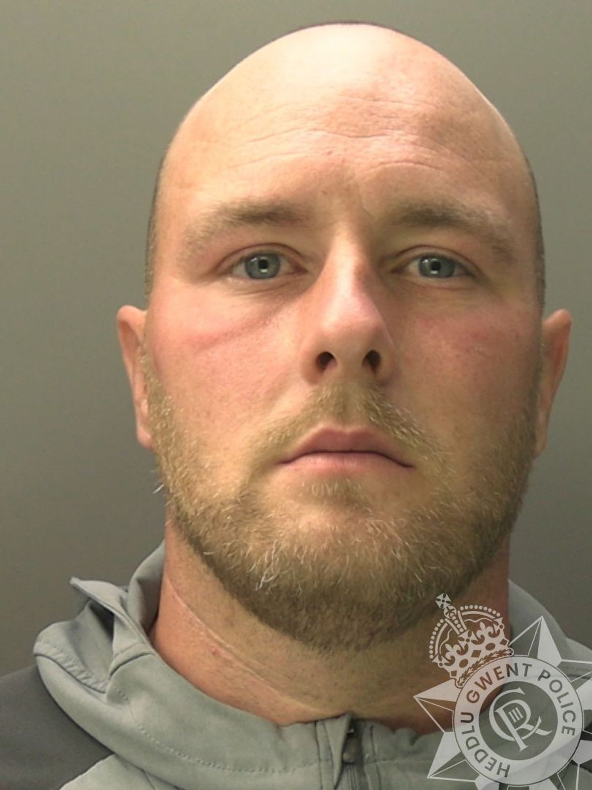 Custody photo of Ryan Battersby, 36, who is bald, has brown stubble and is wearing a grey coat.