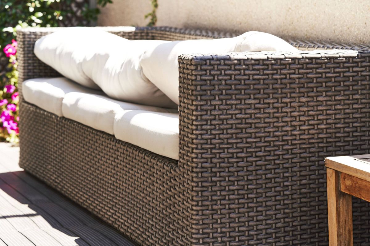 Rattan outdoor sofa with white cushions on sunny patio
