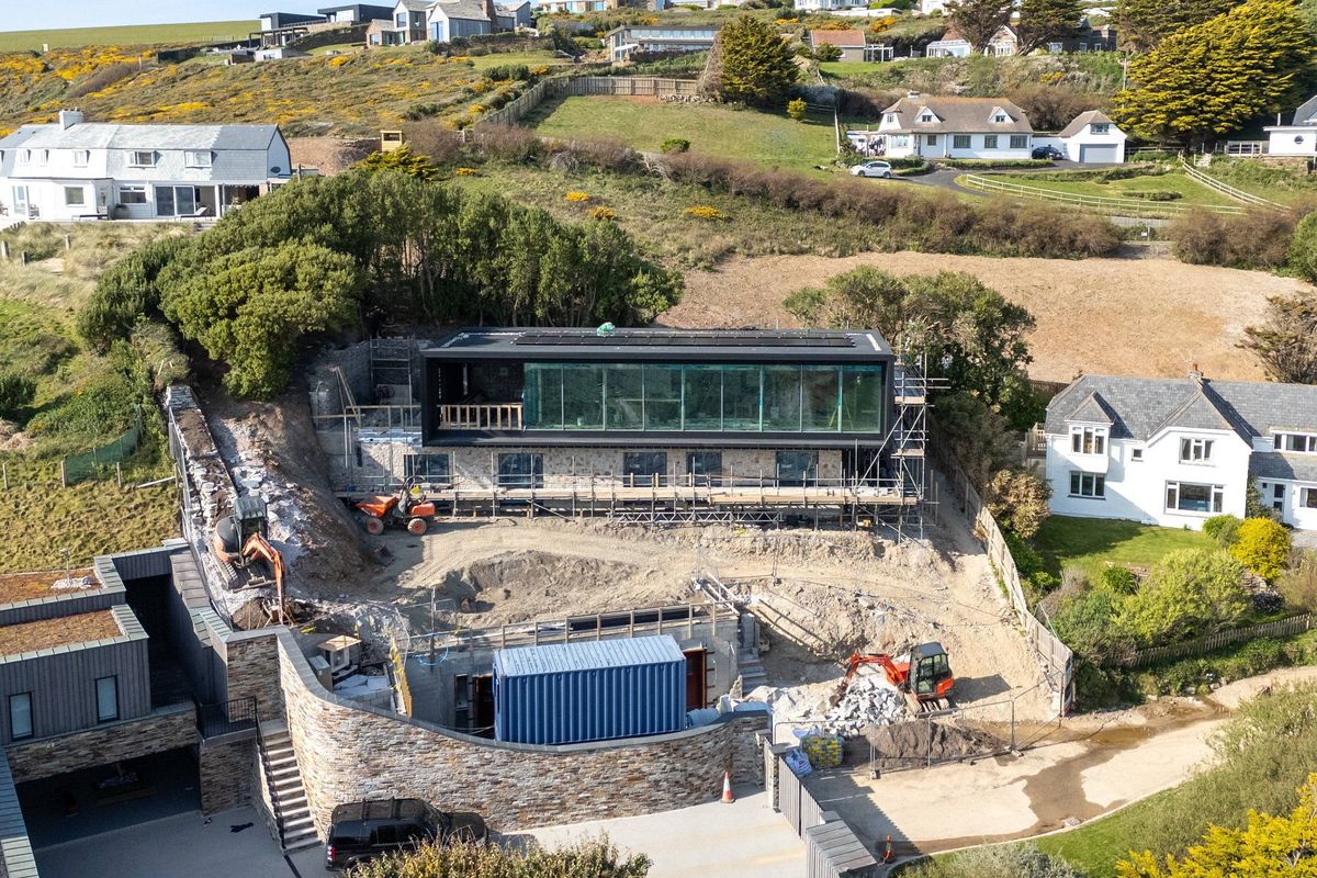 An aerial view of an ongoing construction site featuring a modern architectural design with glass panels set amidst a landscape of residential homes and greenery.