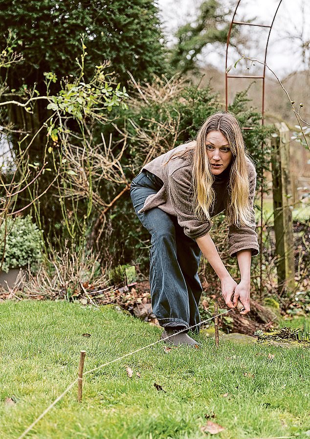 Milli marks out her border garden by placing stakes in the ground at intervals.