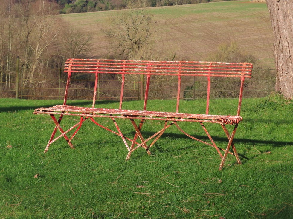 weathered antique arras bench on a grassy area with a background of fields.