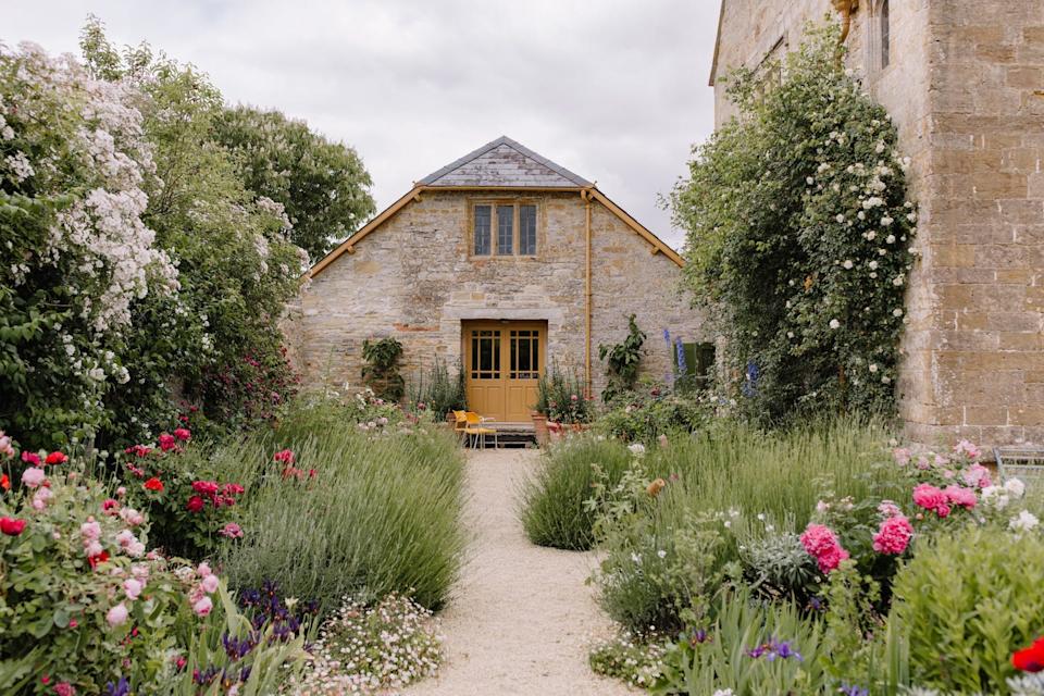 Stone building with a garden pathway and colorful flowers.