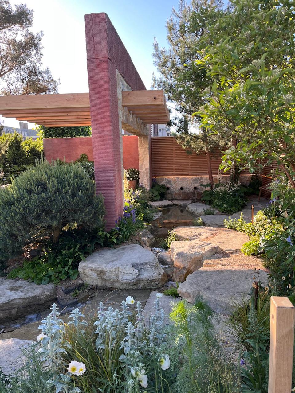 A garden landscape featuring stone elements, greenery, and wooden structures.