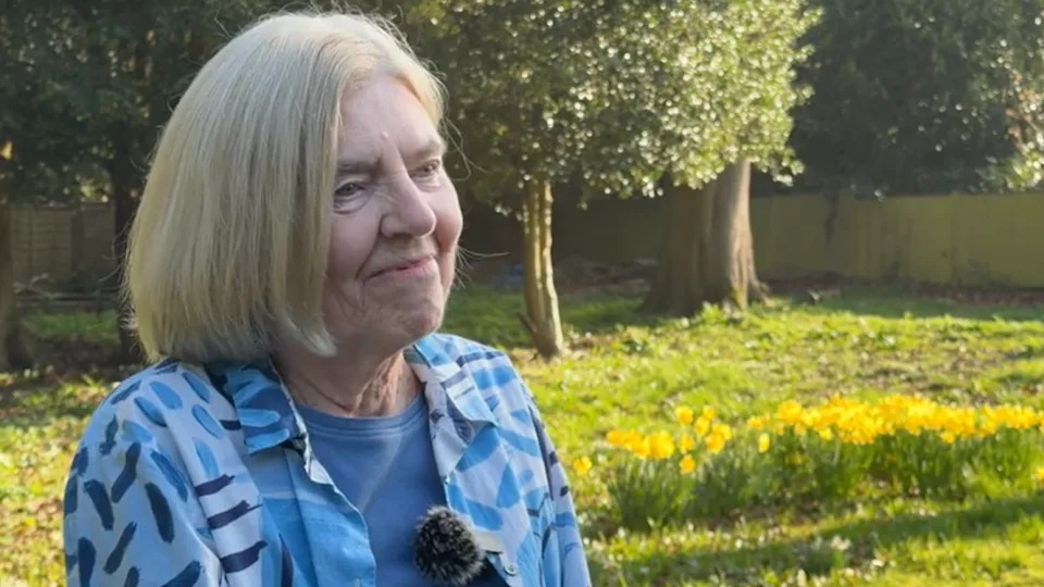 A woman with short blonde hair stood in a garden smiling