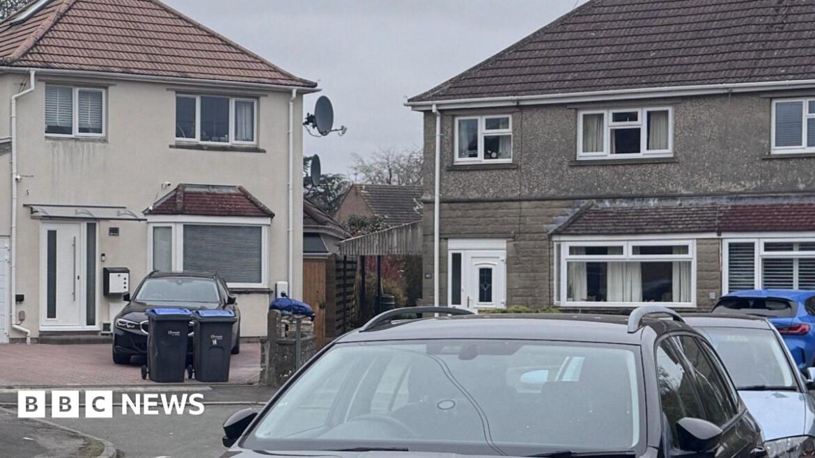Chippenham explosion: Woman dies in ‘gardening accident’ A view of the house from the street. It is a two-storey home with terracotta roof tiles and large driveway, with a white fence on the side of the house leading into the garden. There is another house made of grey brick on the right