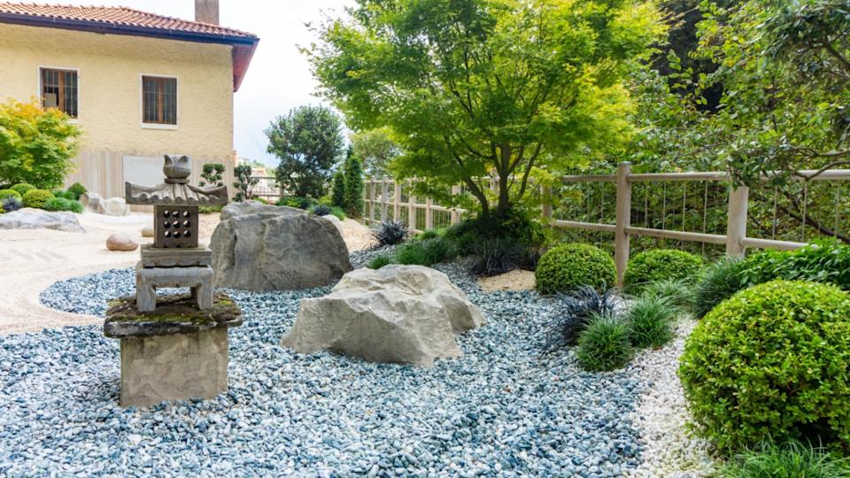 Charming Japanese-style garden with traditional attributes: Oki-gata lantern, gravel paths, boxwood trimmed bushes, maple trees. Landscaping photo of japanese garden.