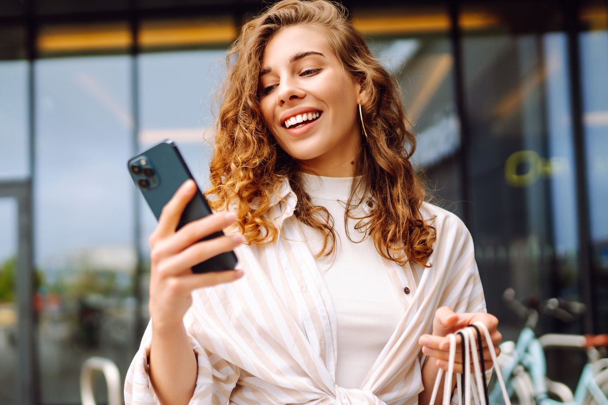 Young Woman use of mobile phone and hold with shopping bag