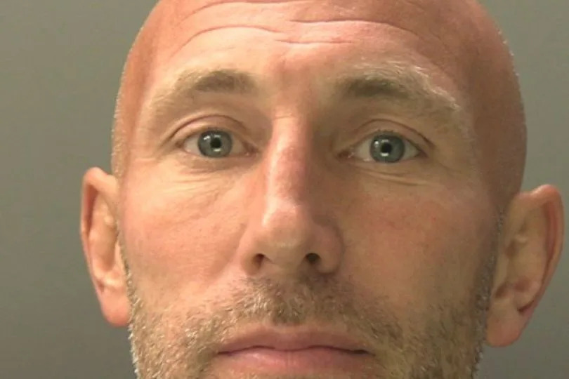 Custody photo of Danny Tomlin, 40, who is bald, has grey stubble and is wearing a black t-shirt.