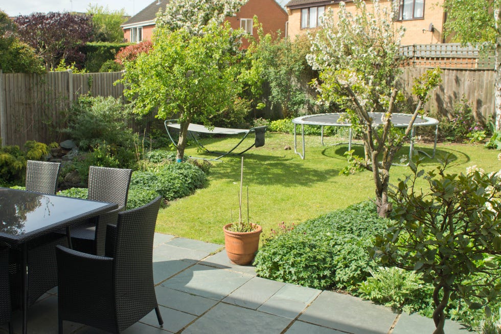 back garden in an english suburban property with chairs and table on a slate patio and a trampoline and a hammock on the lawn in the background.