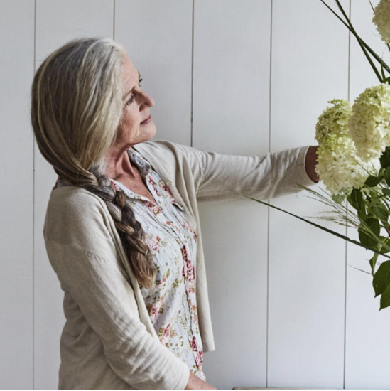 Woman with plaited grey hair and embroidered blouse looking at a floral arrangement
