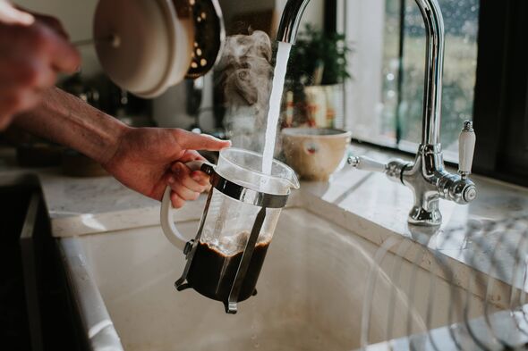 An individual is engaged in the act of pouring water from a faucet into a glass container, situated within a kitchen environment