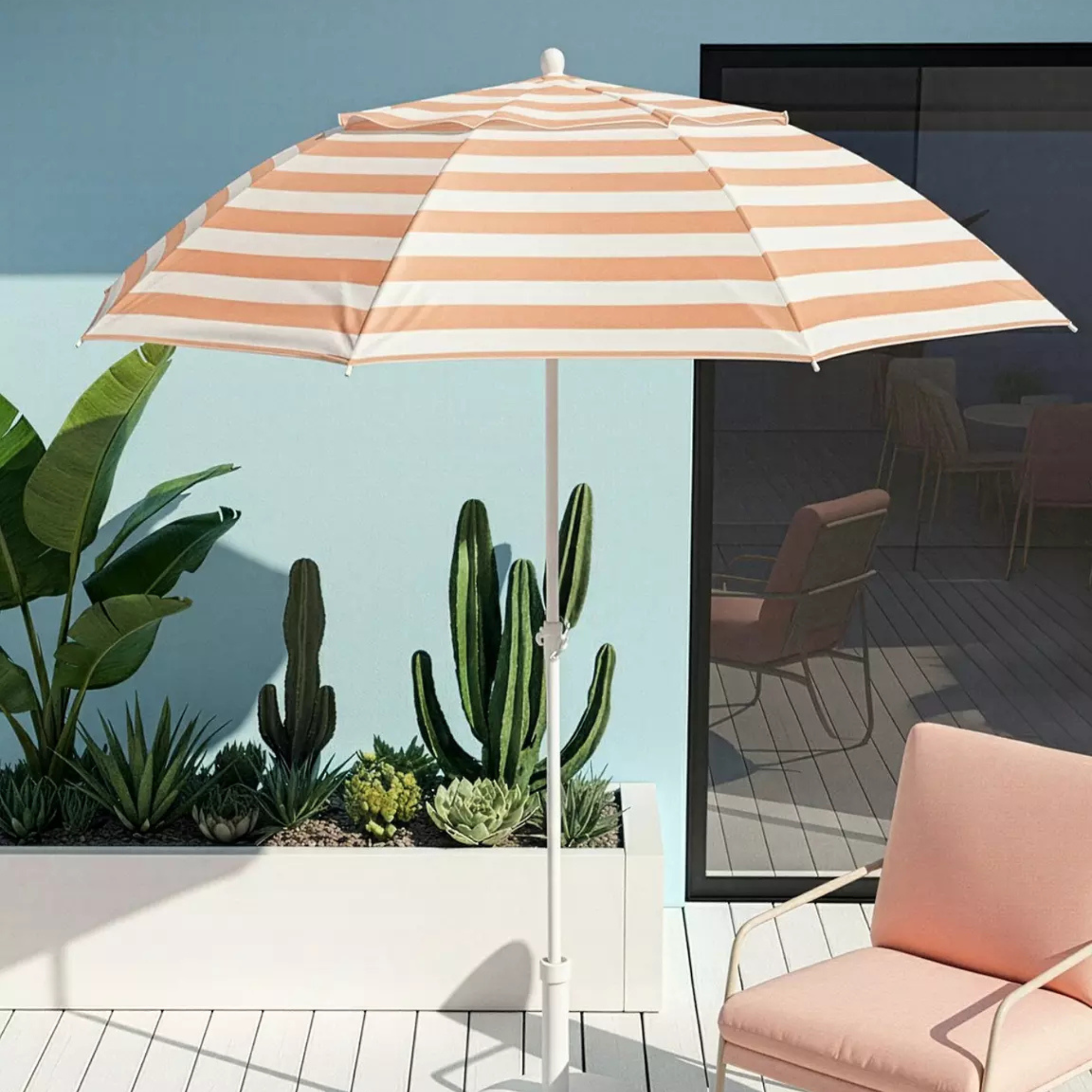 Very peach striped parasol in front of blue wall and a peach chair.