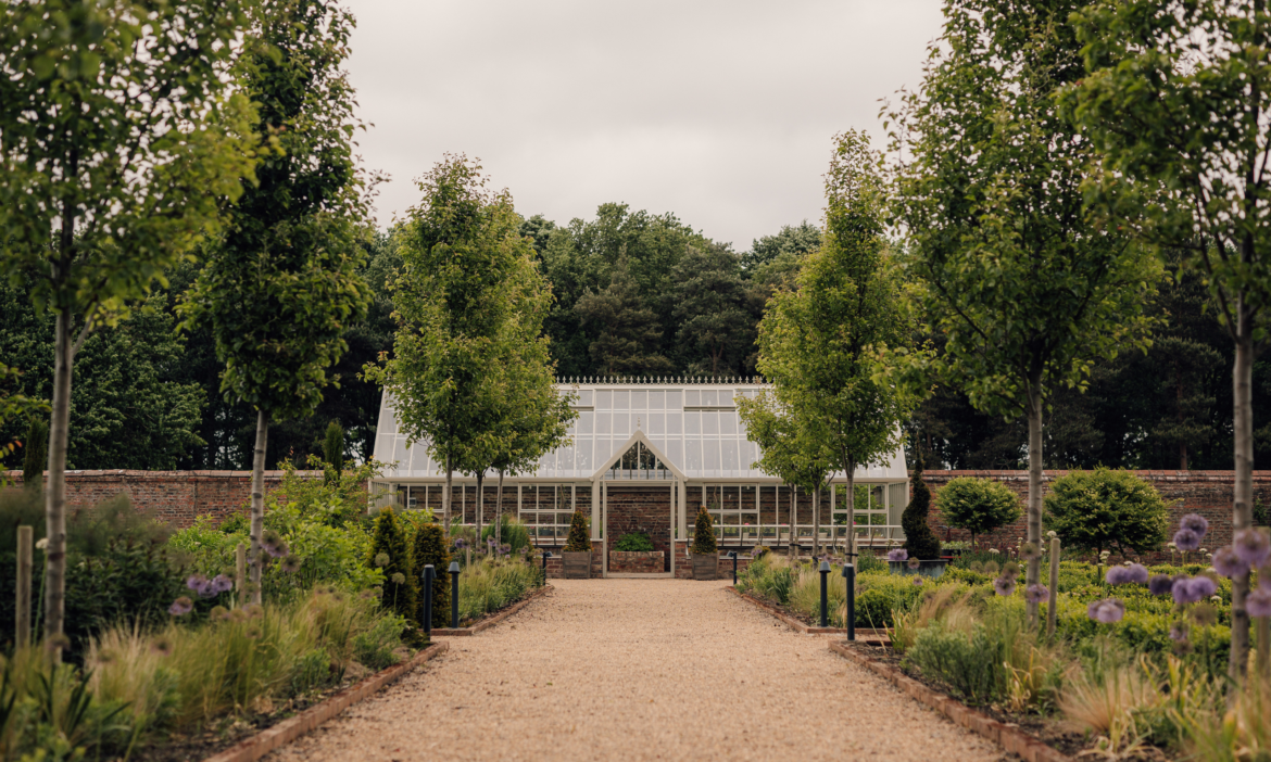 Greenhouse at the end of a wide gravel path in a walled garden