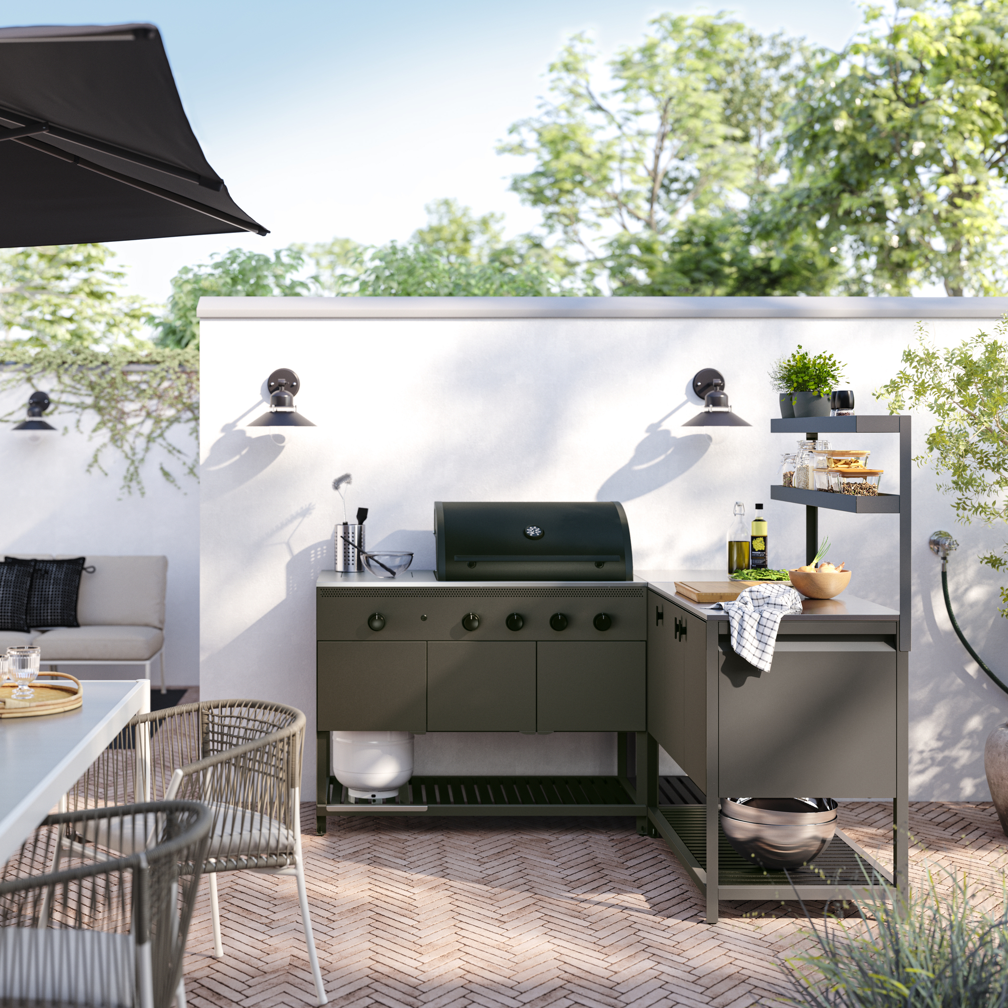 Image of an outdoor patio with brick floors and a white wall. There is a dark gray grill and a matching cabinet/countertop connected to it.