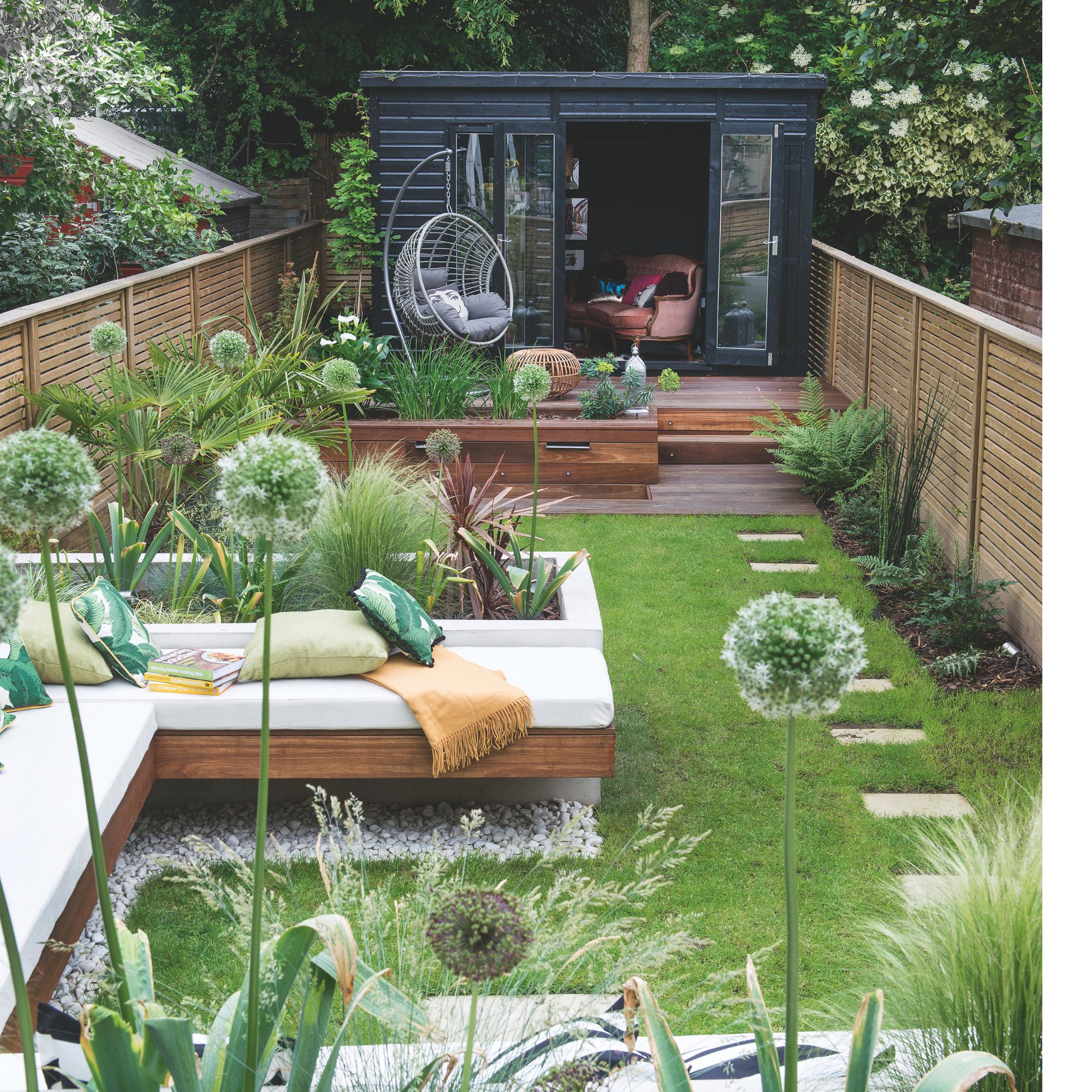 Small garden with lawn, stepping stones, hanging egg chair and garden room next to decking area