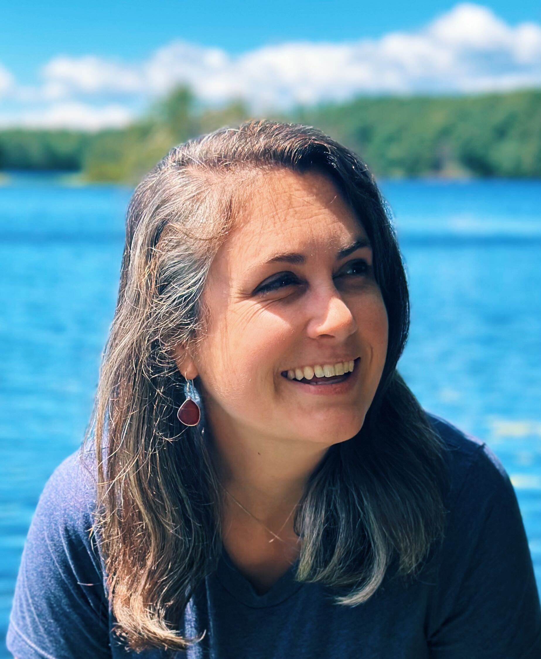 woman smiling wearing blue top with the natural landscape behind her