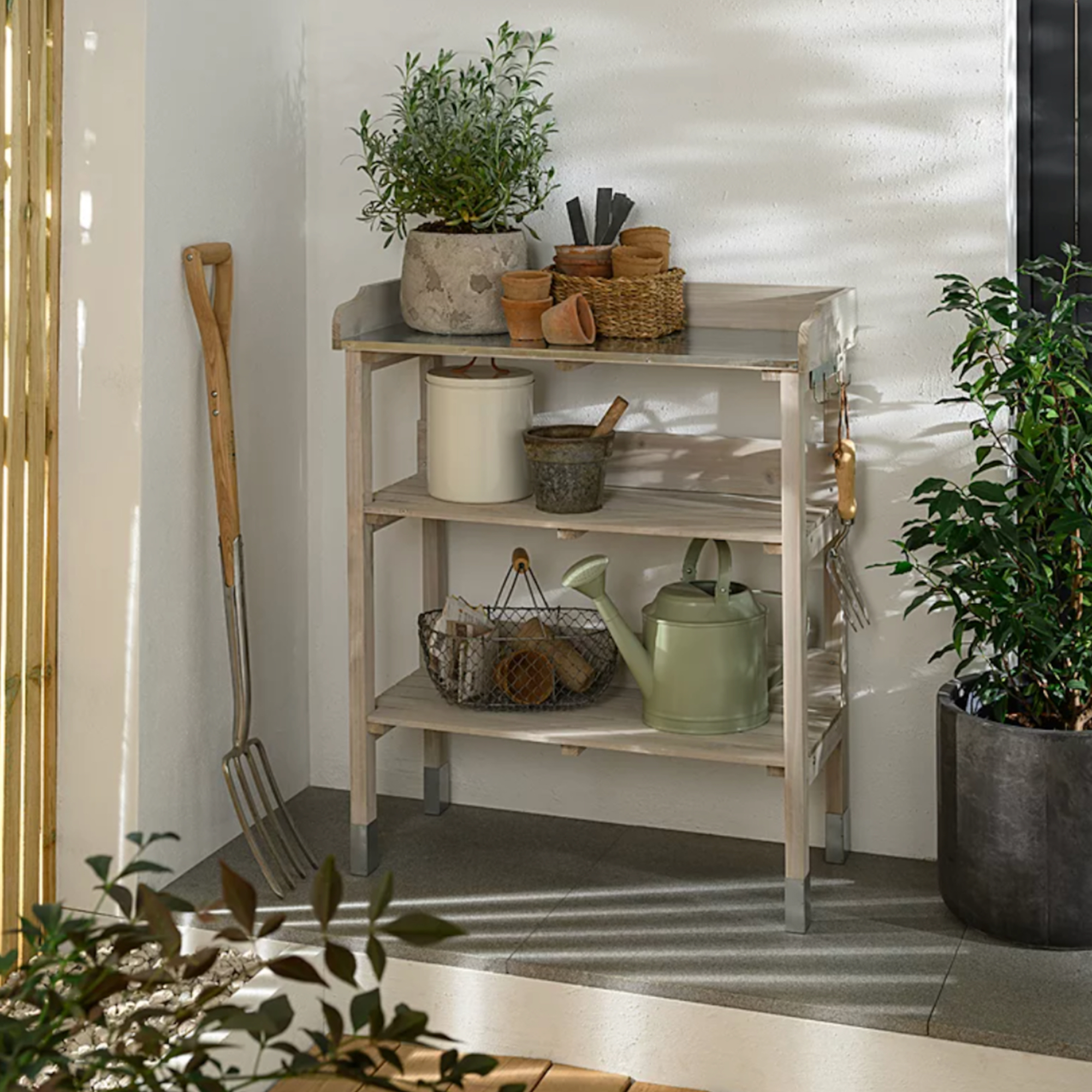 potting bench with terracotta pots, metal rug, watering can and fork propped up on the side